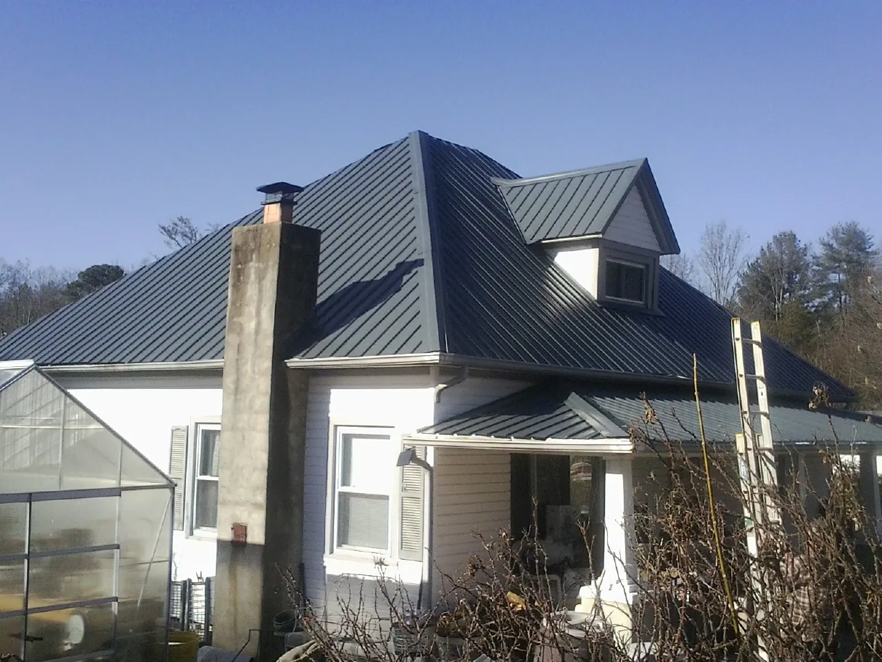 Dark blue standing seam metal roof on a white farmhouse with dormer — Slate & Tile Roof Repair by Roofing Brothers in Rosholt