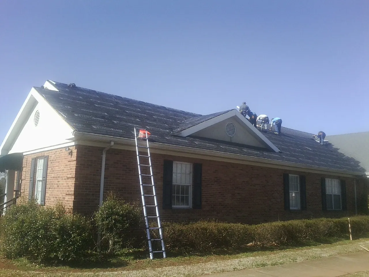 Crew tearing shingles off a brick ranch roof with a ladder set — Emergency Roof Repair work by our crew in Rosholt