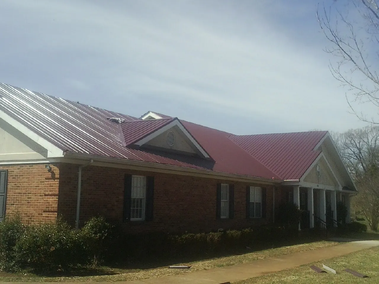 Red metal roof with gabled entries on a long brick building, from a Hail Damage Roof Repair job in Rosholt