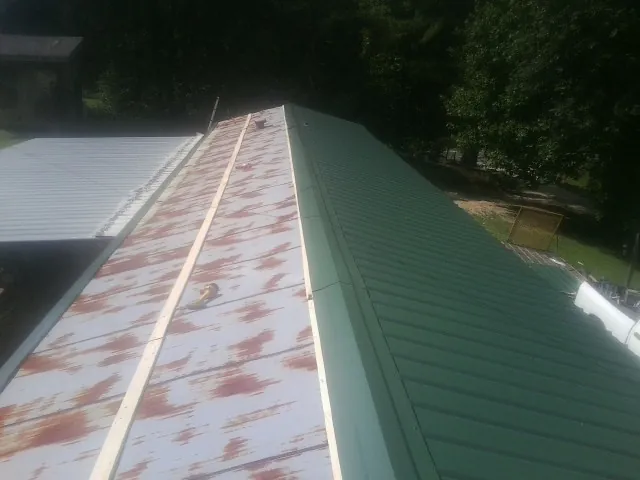 Old rusted panels beside newly installed green metal roofing in Rosholt