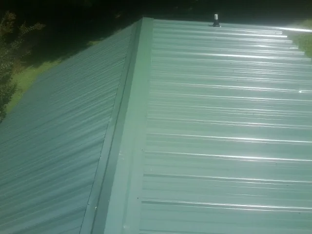 New green metal panels meeting at the ridge of a roof — Flat Roof Repair work by our crew in Rosholt